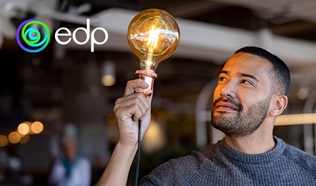 Homem sorridente segura numa lâmpada acesa com o símbolo da EDP ao lado na imagem.